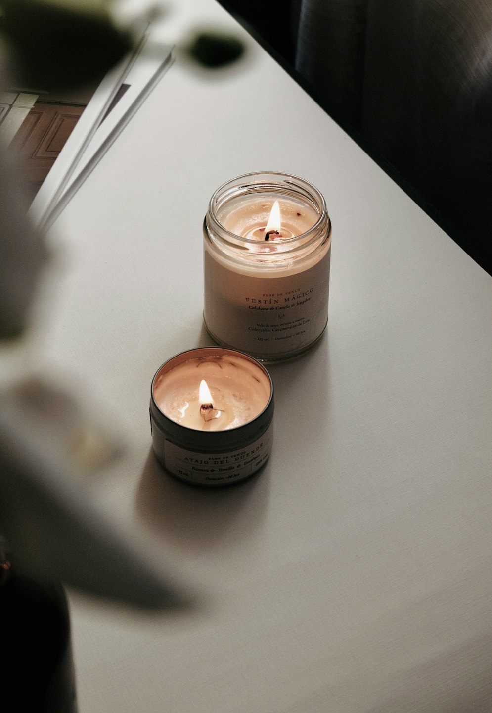 Two burning scented candles on a light-colored surface.