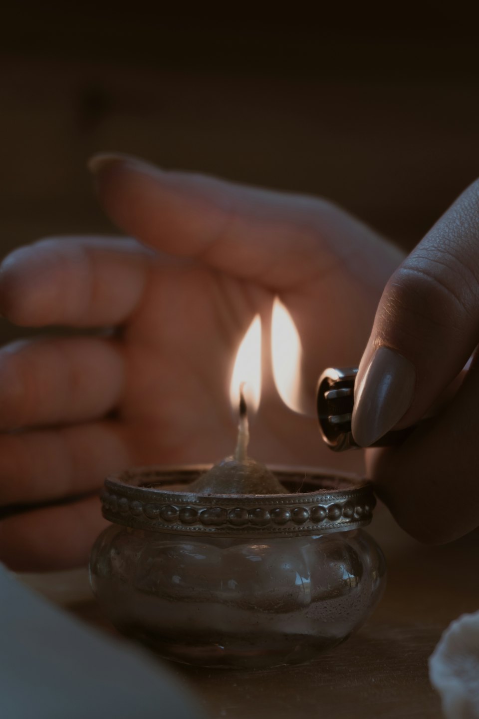 Hands lighting an ornate candle with a silver rim.