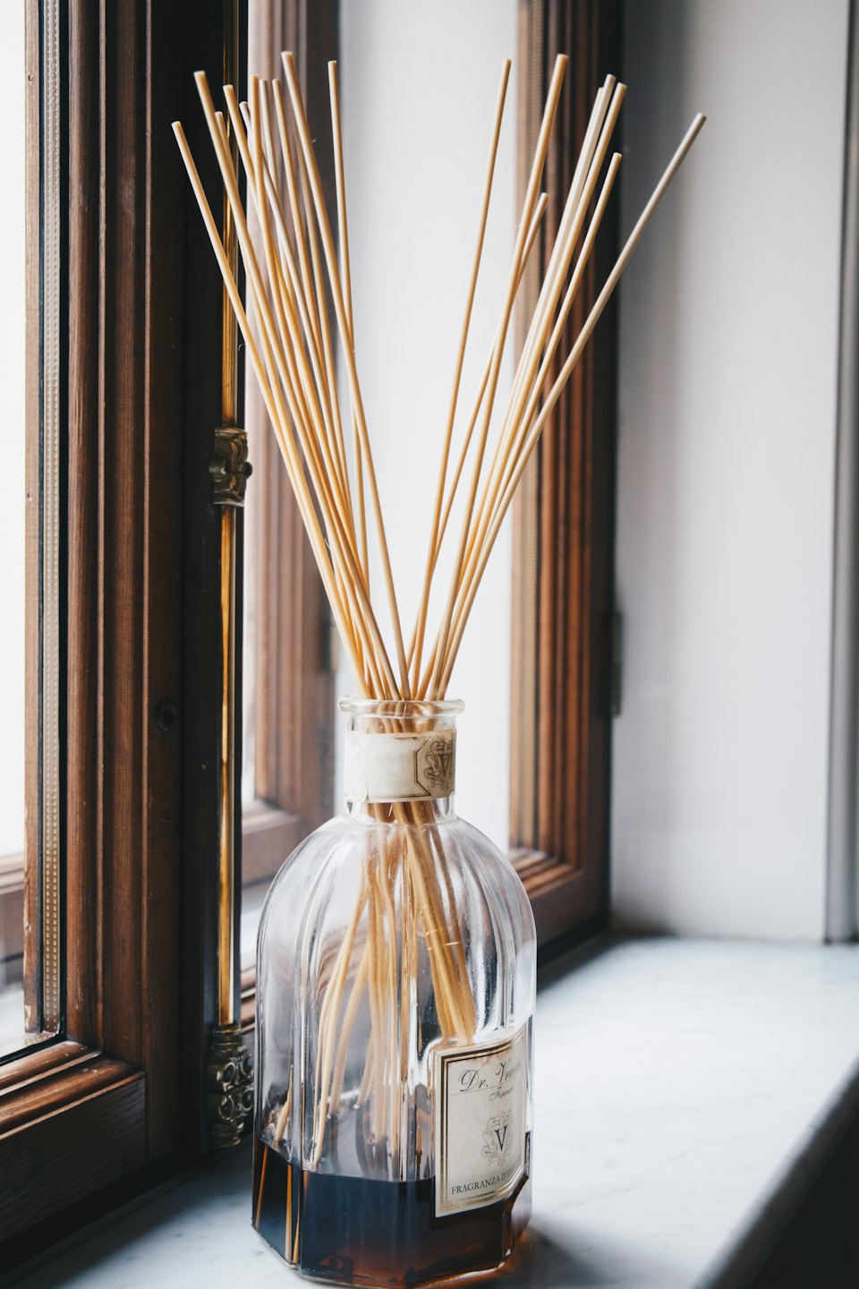 Reed diffuser with dark brown oil on marble windowsill.