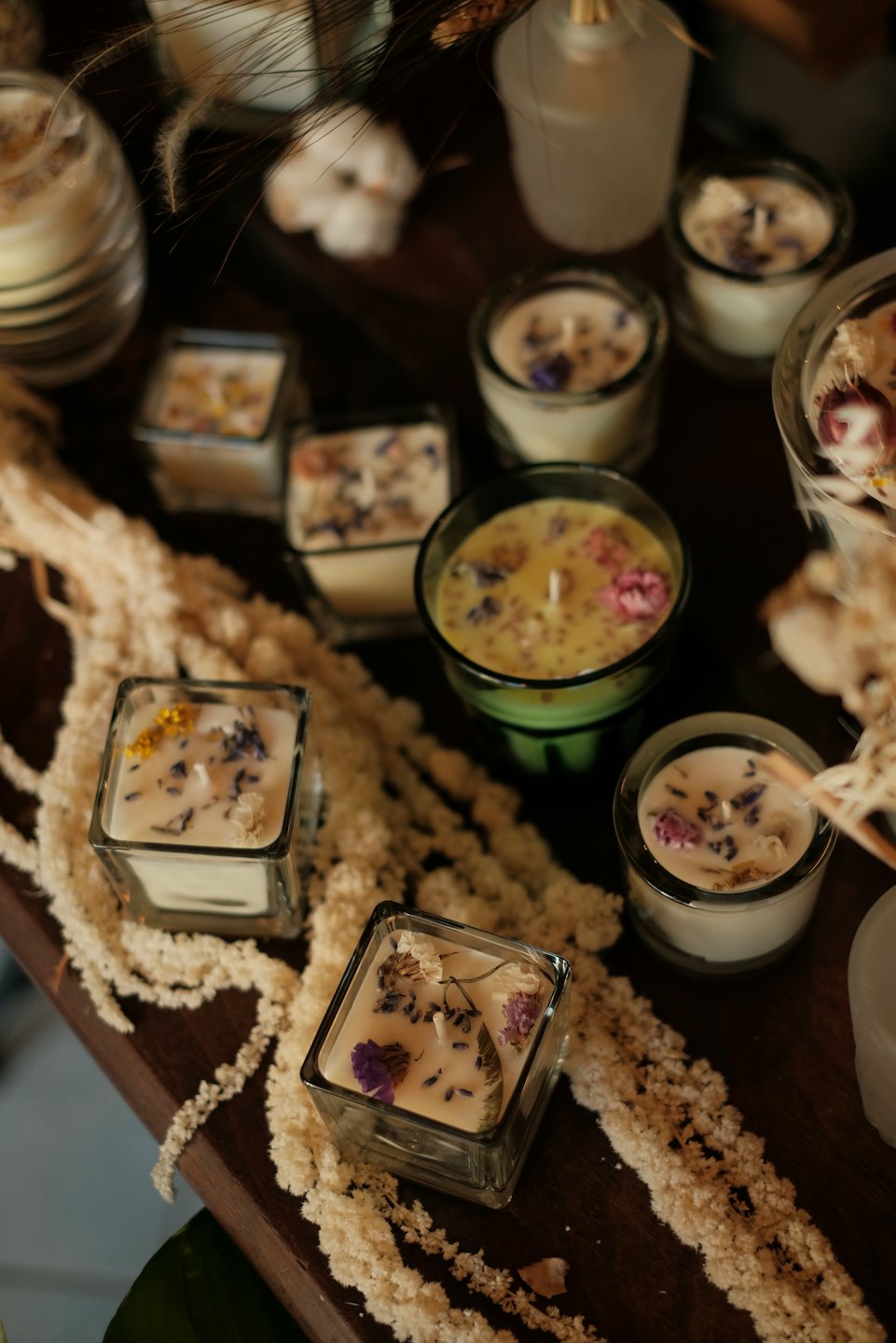 Handcrafted soy wax candles with dried flowers on wood.